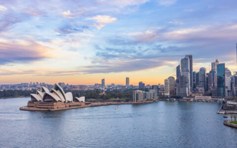 Sydney Opera House at sunset with passenger boat in foreground and city skyline in background viewed from Harbour Bridge